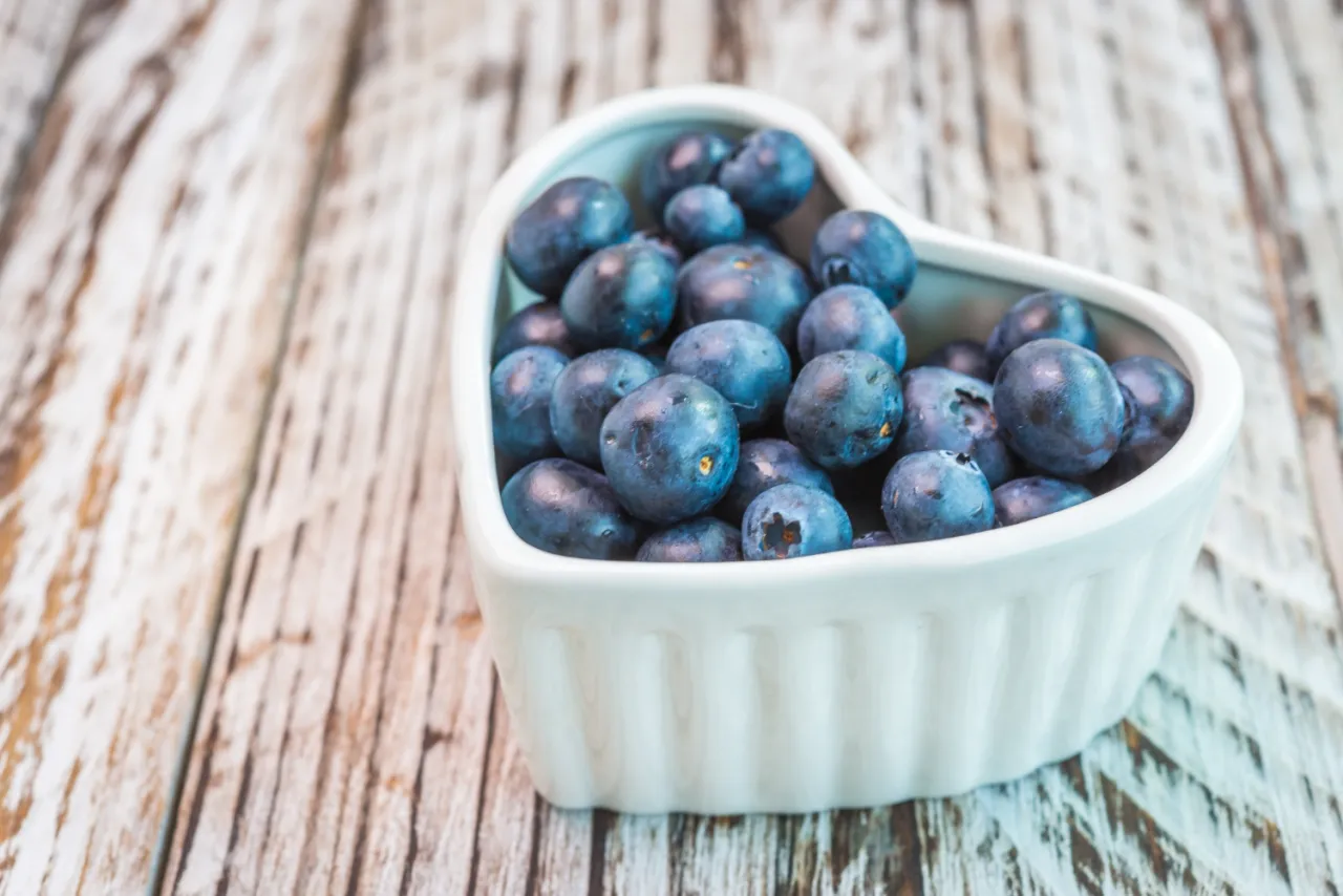 Serce pełne bor&oacute;wek amerykańskich w ciąży. Zdrowe owoce w białej miseczce na drewnianym tle.