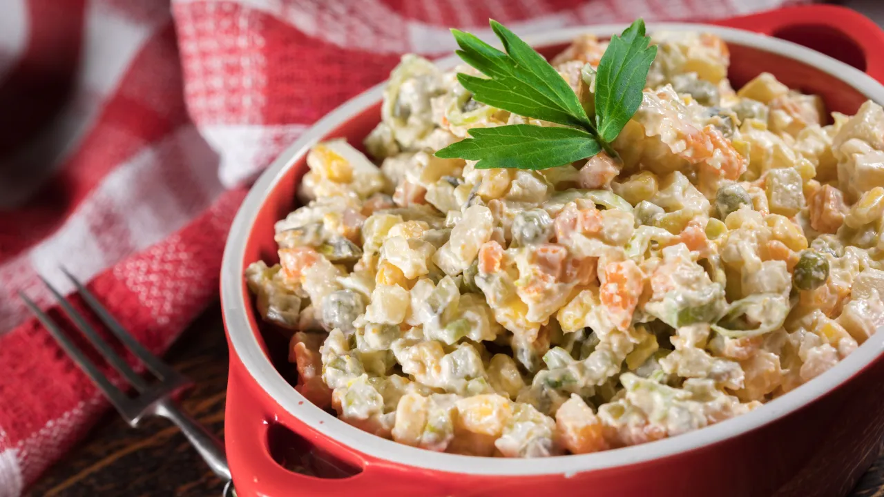 Sałatka jarzynowa w czerwonej misce, udekorowana natką. Zastanawiasz się, ile może stać sałatka jarzynowa w lodówce?