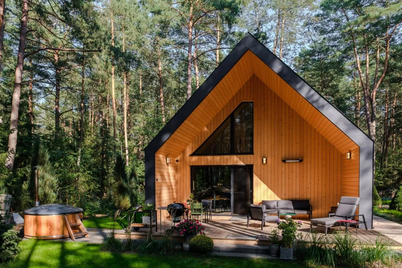 Nowoczesny dom drewniany w lesie z bali, z tarasem, jacuzzi i grillem. Zastanawiasz się, ile kosztuje budowa domu drewnianego pod klucz?