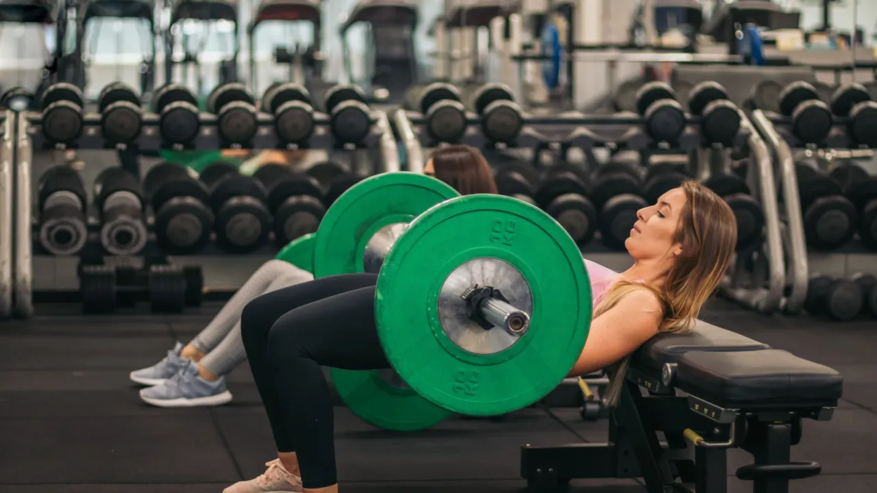 Kobiety ćwiczą hip thrusty z obciążeniem, by wzmocnić pośladki. Ile razy w tygodniu ćwiczyć pośladki? To zależy od cel&oacute;w i regeneracji.
