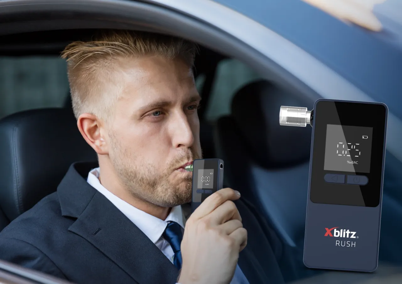 Mężczyzna w garniturze dmucha w alkomat, by sprawdzić, ile może wypić. Wynik 0.25 %BAC.