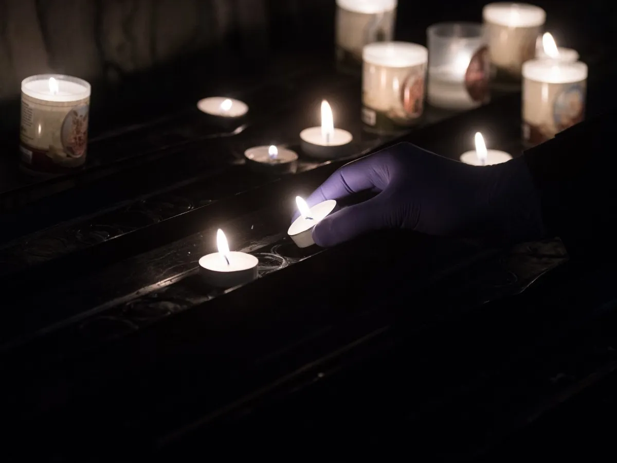 Ręka w rękawiczce zapala świecę. Wiele płonących świateł, jak 5 przykazań kościelnych, tworzy mistyczną atmosferę.