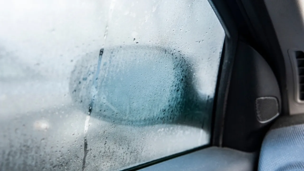 Krople na szybie samochodu, odbicie lusterka. Włączony nawiew daje zimne powietrze, kt&oacute;re osadza się na szybie.