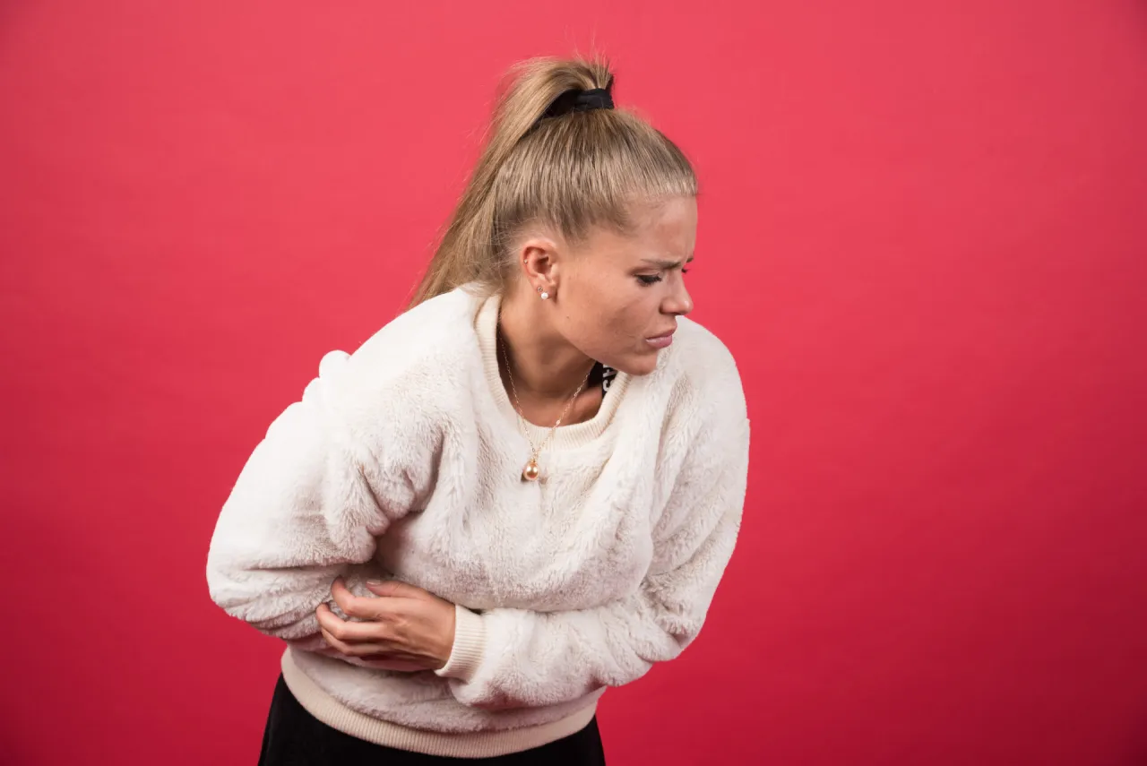Kobieta z b&oacute;lem brzucha, szuka czegoś, co pomaga na b&oacute;l brzucha.