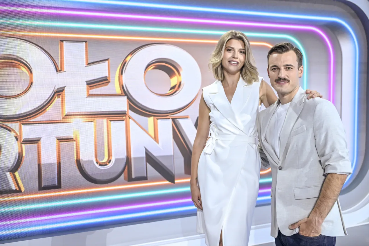 Para, która prowadziła Koło Fortuny, pozuje na tle neonowego logo programu.
