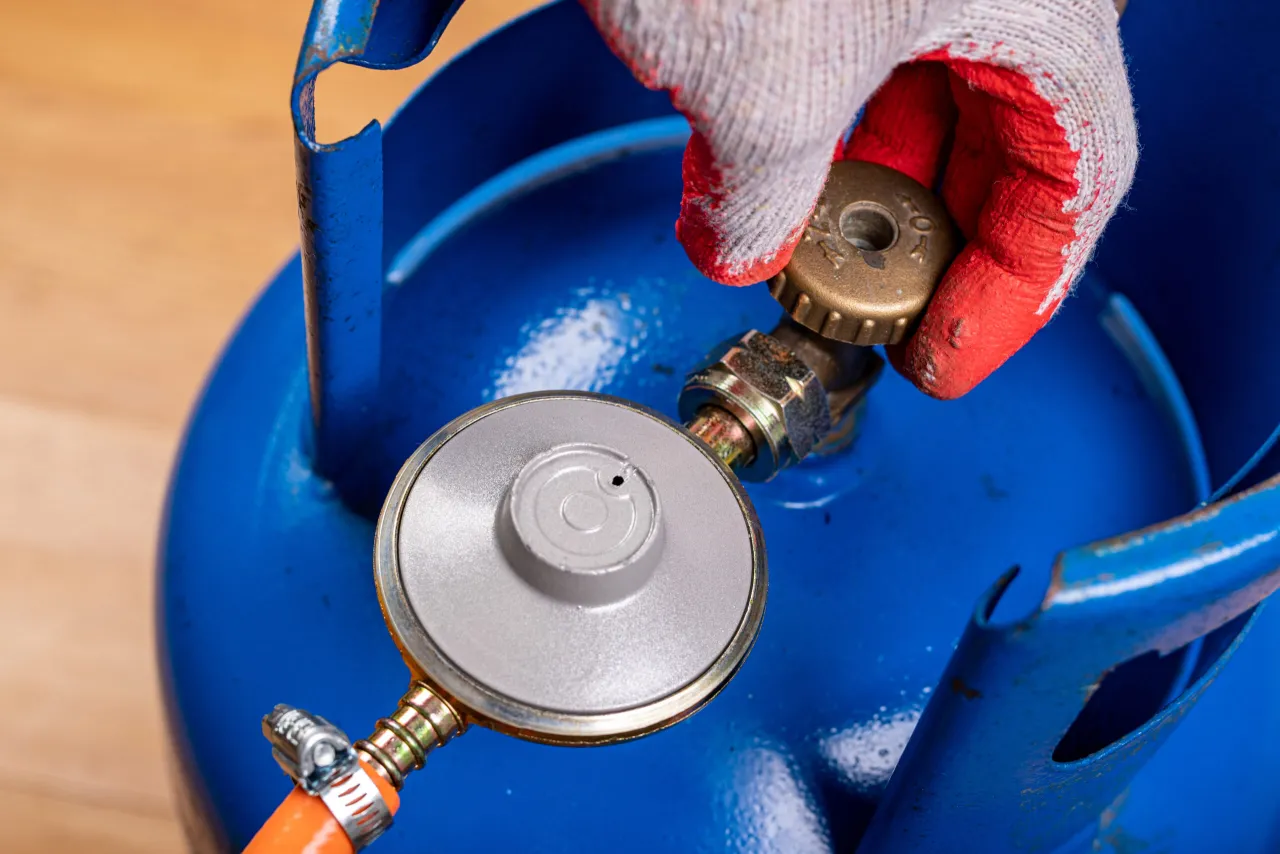 Ręka w rękawicy dokręca zaw&oacute;r do butli gazowej. Widać reduktor gazu z uszczelką, gotowy do podłączenia.