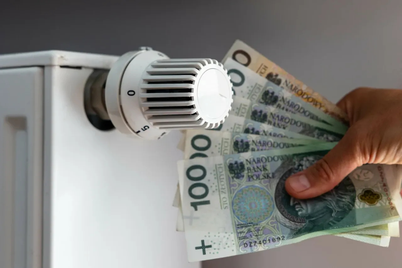 Dłoń trzyma banknoty 100 zł przy grzejniku. Zastanawiasz się, jak uzyskać dofinansowanie do węgla?