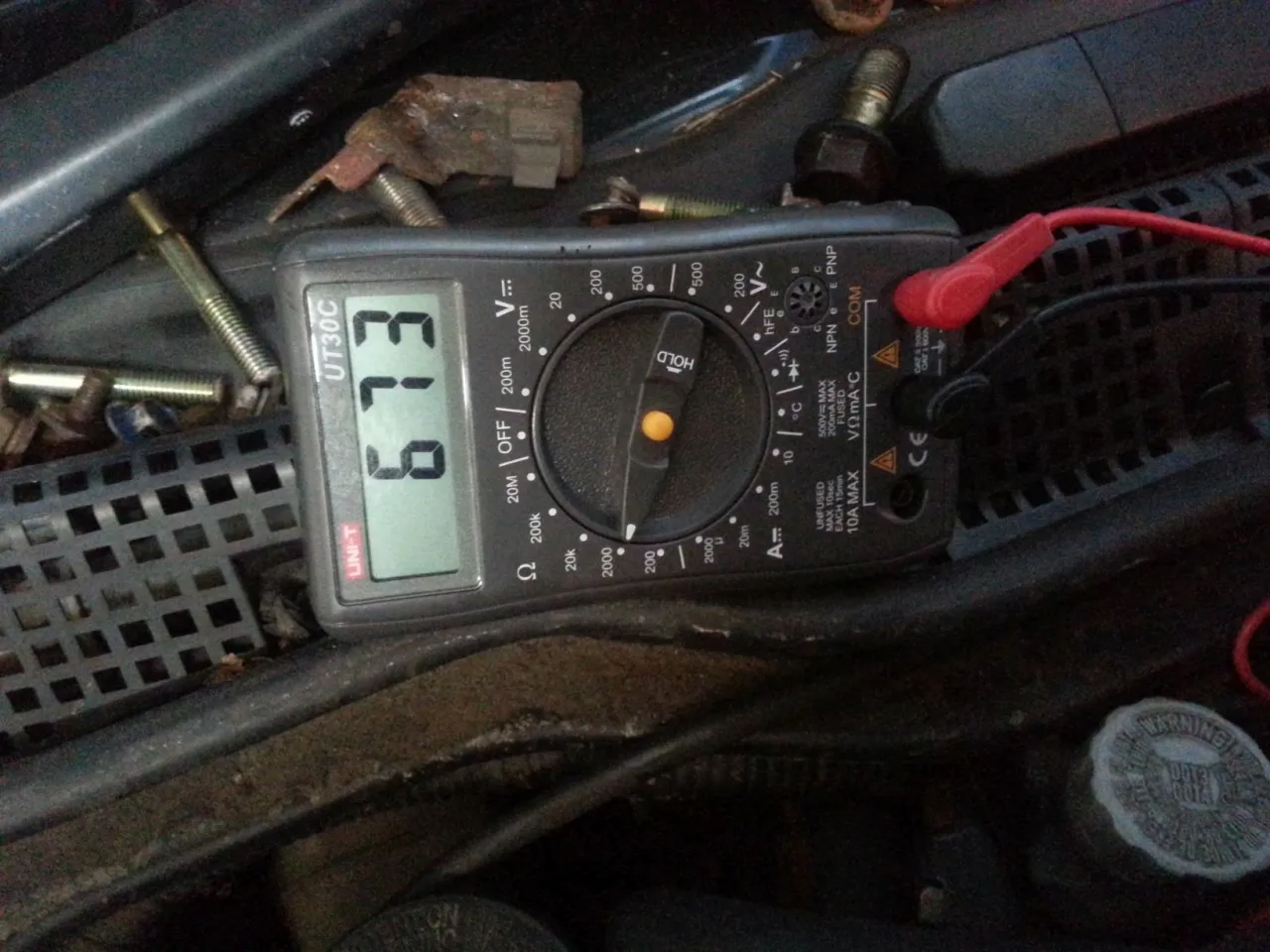 Multimetr pokazuje 6.13 Ω, co jest kluczowe, jak sprawdzić czujnik ABS. Widać przewody i elementy silnika.