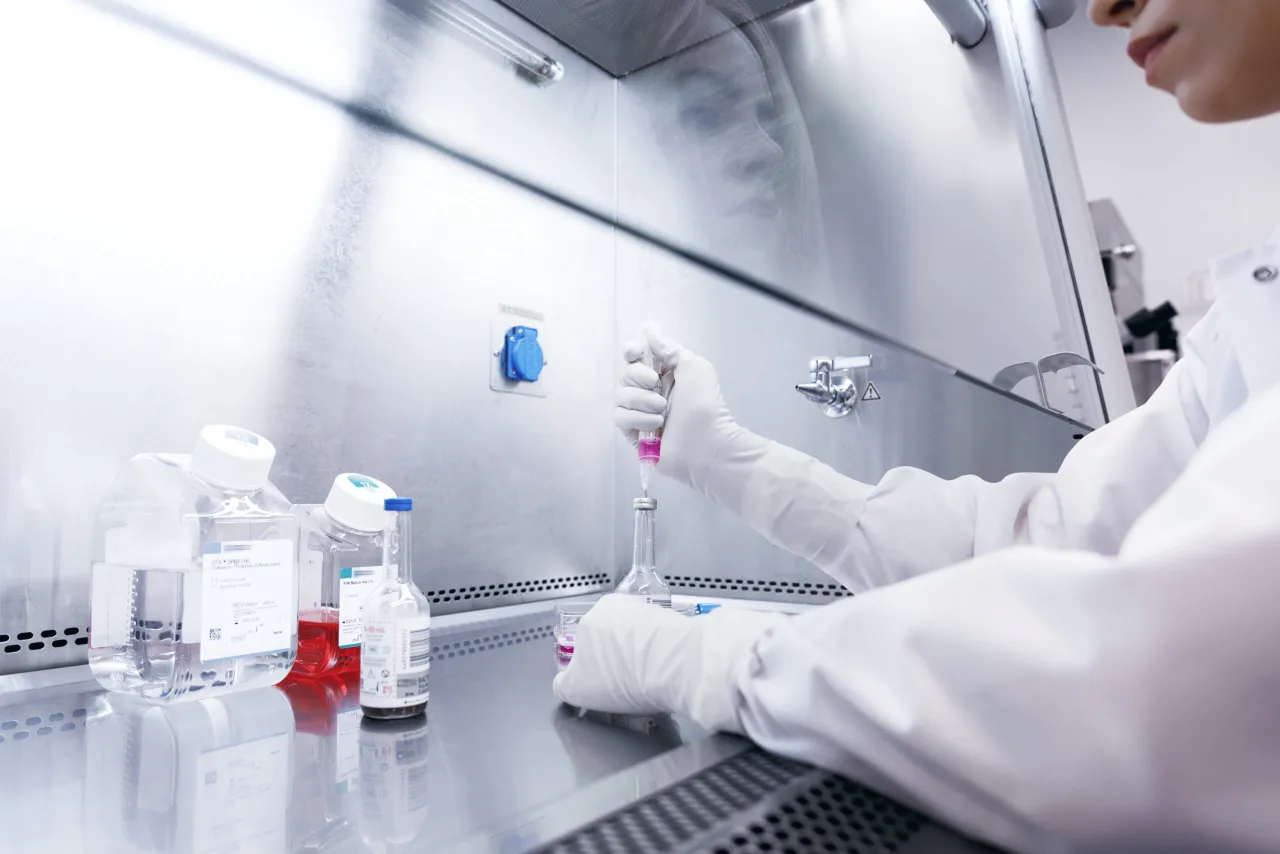 W sterylnym laboratorium, gdzie diagnostyka to klucz do sukcesu, pracownik w białym fartuchu i rękawiczkach precyzyjnie pobiera próbkę różowego płynu.