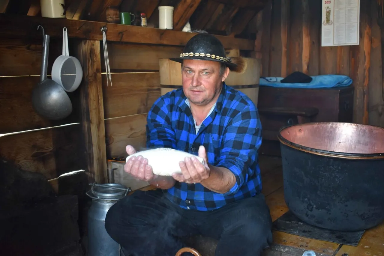 Mężczyzna w tradycyjnym stroju, w bacówce, trzyma w dłoniach ser.