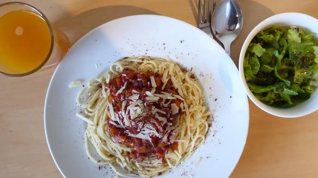 Teller mit Spaghetti Bolognese und einem kleinen Beilagensalat daneben