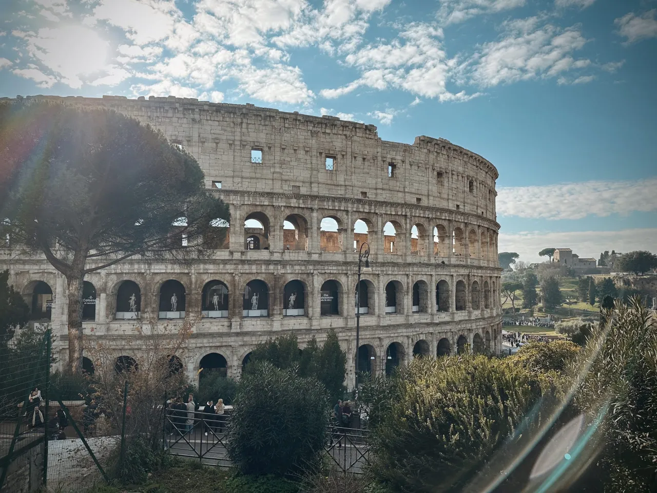 Koloseum w Rzymie, idealne na zwiedzanie w 4 dni. Słońce przebija się przez chmury, oświetlając antyczne mury i otaczającą zieleń.