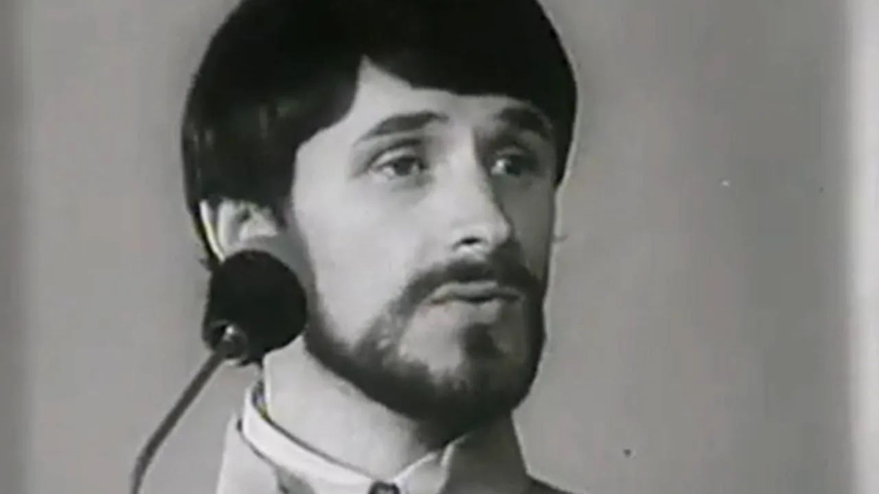 Mężczyzna z brodą i wąsami, w jasnej marynarce, śpiewa do mikrofonu. Może to być wspomnienie z dzikiej plaży.