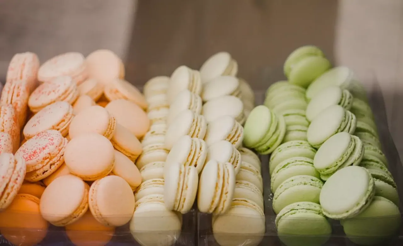 Kolorowe makaroniki, idealne na to, co kupić w Paryżu. Różowe, białe i pistacjowe słodkości piętrzą się w gablotach.