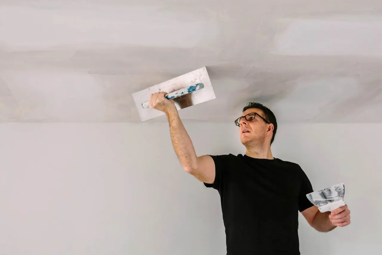 Mężczyzna w okularach uczy się, jak tynkować sufit, używając kielni i packi.