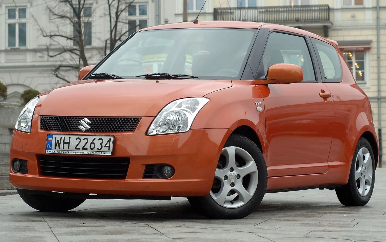 Pomarańczowy Suzuki Swift, pierwszy samoch&oacute;d z salonu, stoi na ulicy.