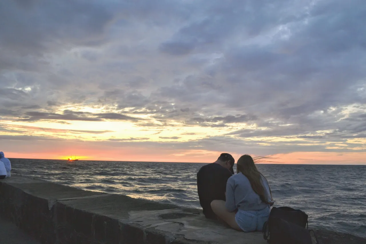 Para szuka tanich wczasów nad morzem dla 2 osób z wyżywieniem, podziwiając zachód słońca i żaglowiec.