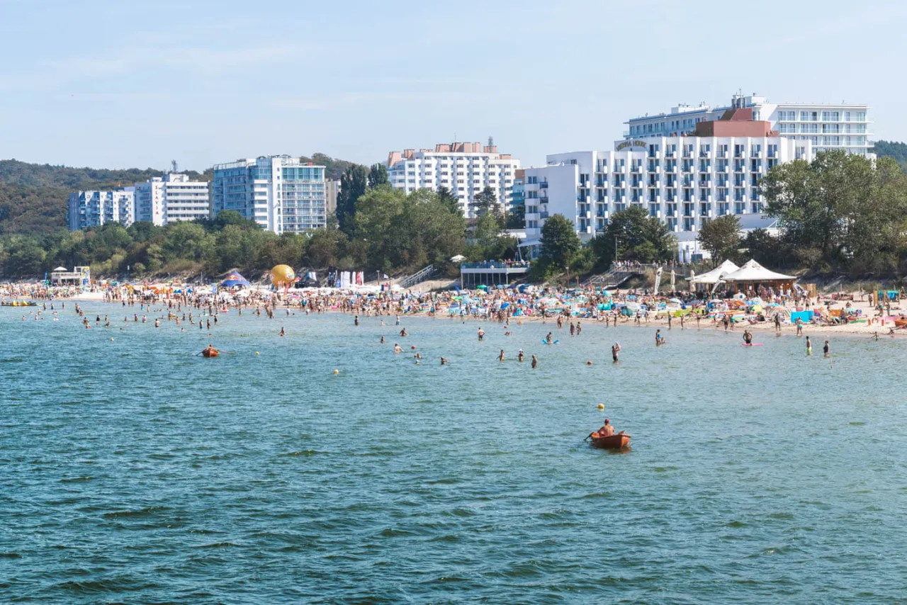 Tłum ludzi na plaży i w morzu, hotele w tle. Idealne miejsce, by sprawdzić, co zwiedzić w Międzyzdrojach.