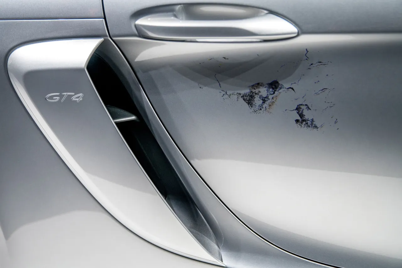Uszkodzony lakier na srebrnym Porsche GT4, widoczne odpryski i łuszczenie się farby. To pokazuje, dlaczego schodzi lakier z samochodu.