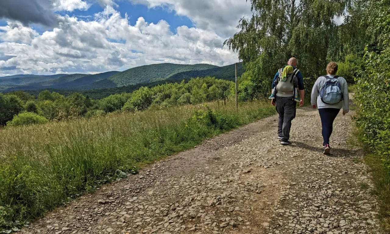 Rodzina wędruje szlakiem w kierunku bac&oacute;wki PTTK pod Małą Rawką. Malownicze Bieszczady w tle.
