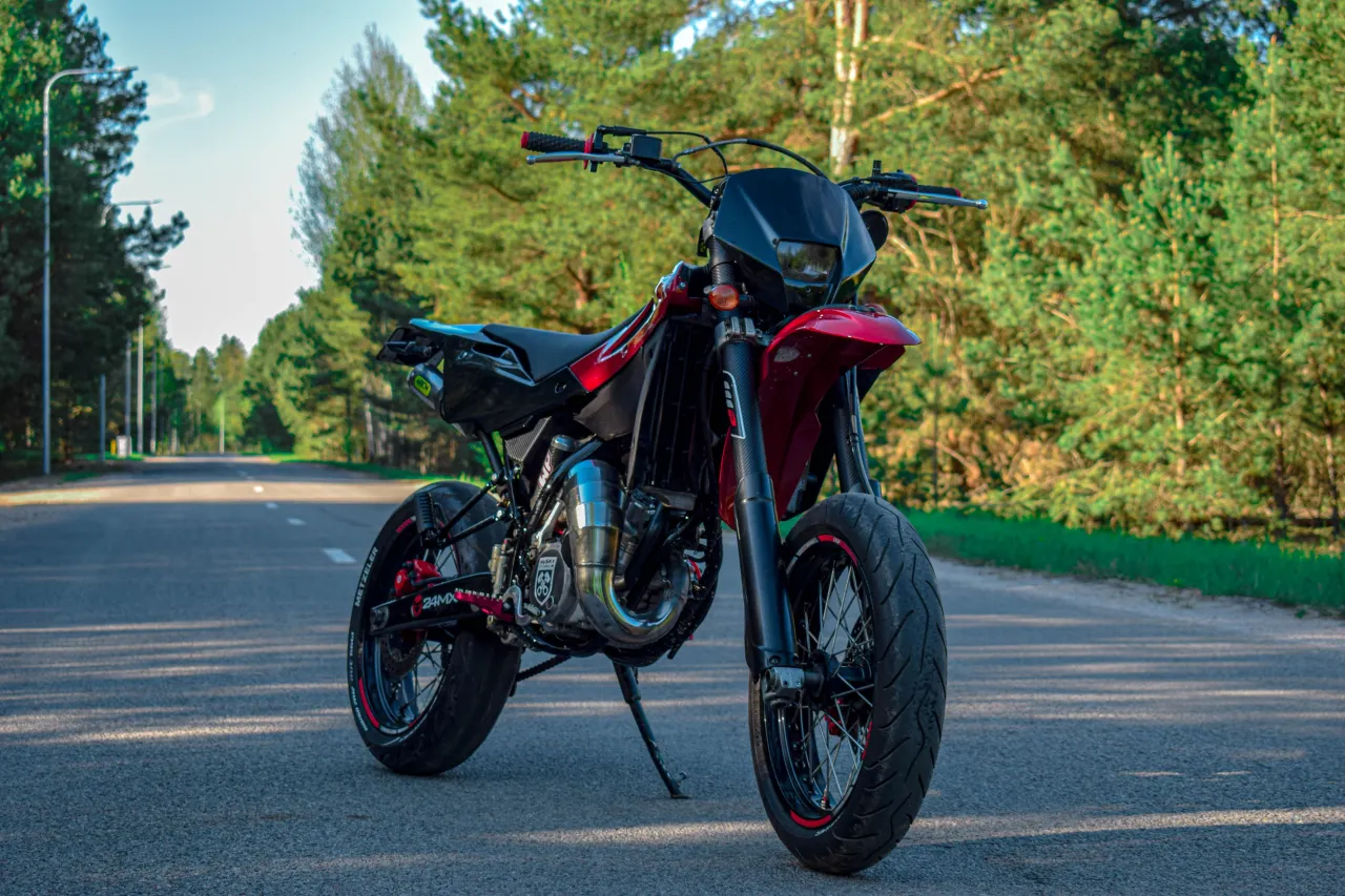 Czerwony Husqvarna SM 125 na tle leśnej drogi.