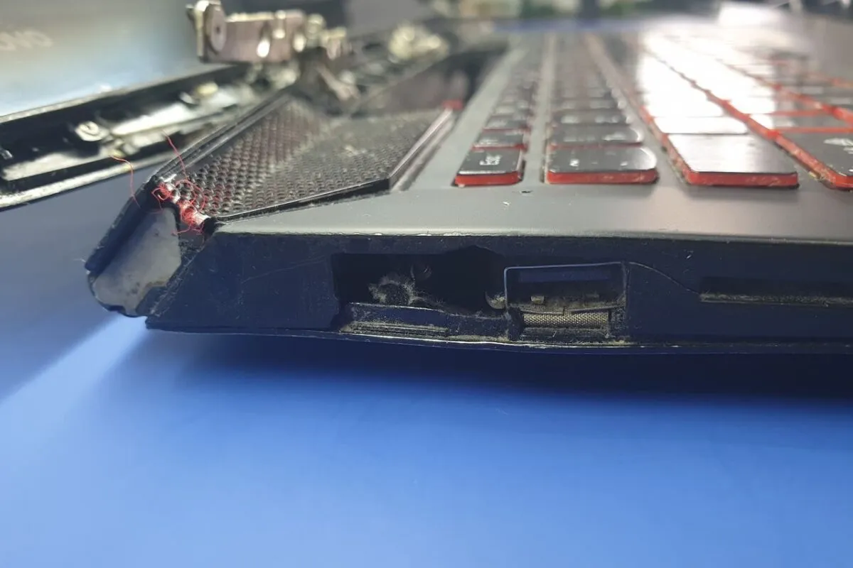 Uszkodzona bateria w laptopie objawy: wybrzuszenie obudowy, widoczne pęknięcia i luźne elementy. Widać też kurz i brud wewnątrz.