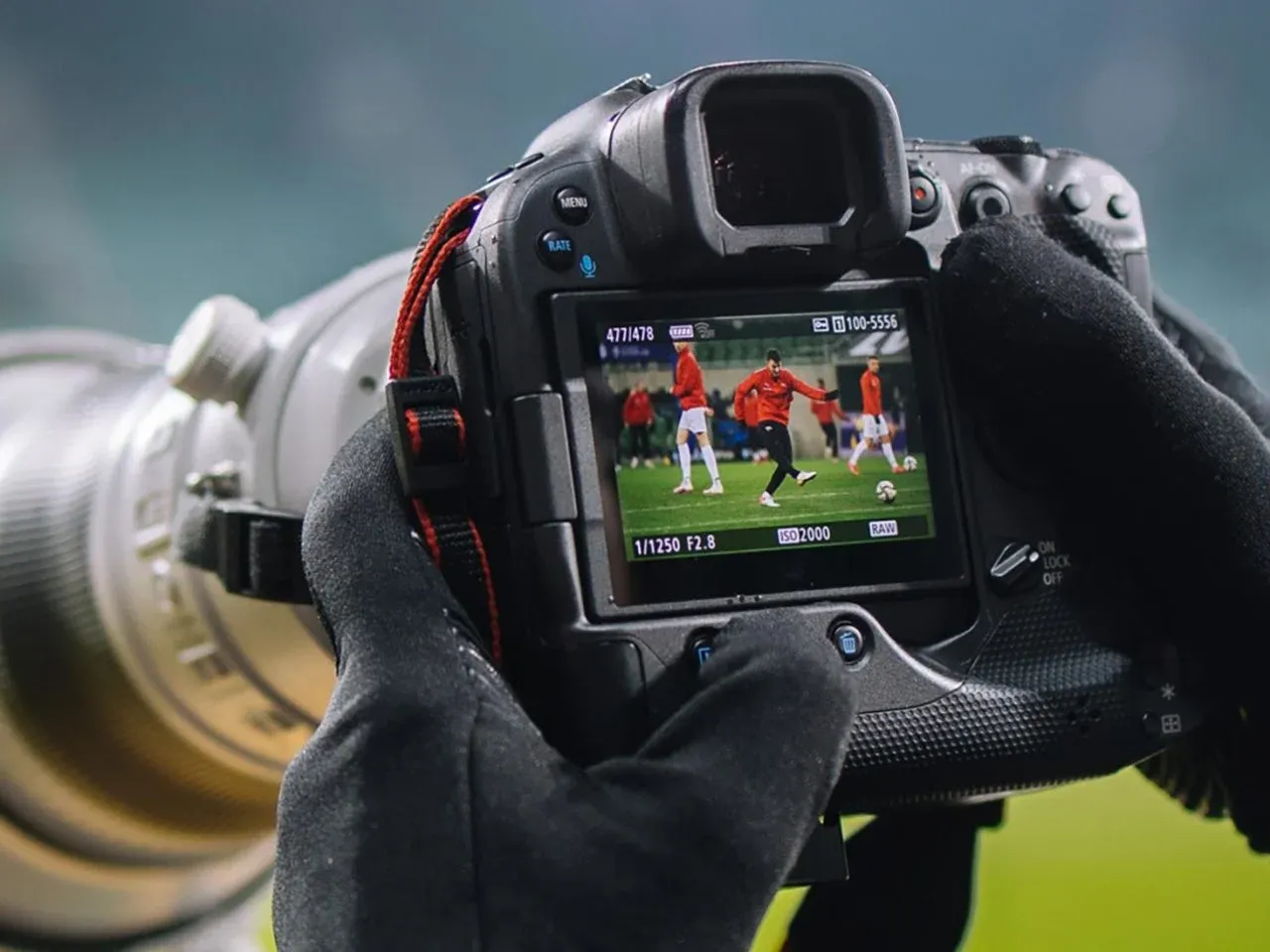 Ręce w rękawiczkach trzymają lustrzankę dla początkujących, rejestrując trening piłkarski.