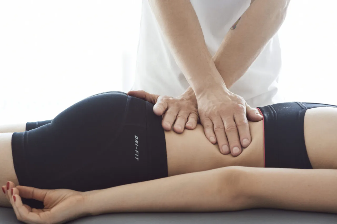 Fizjoterapeuta masuje dolną część pleców pacjentki. Długość rehabilitacji kręgosłupa lędźwiowego zależy od schorzenia.