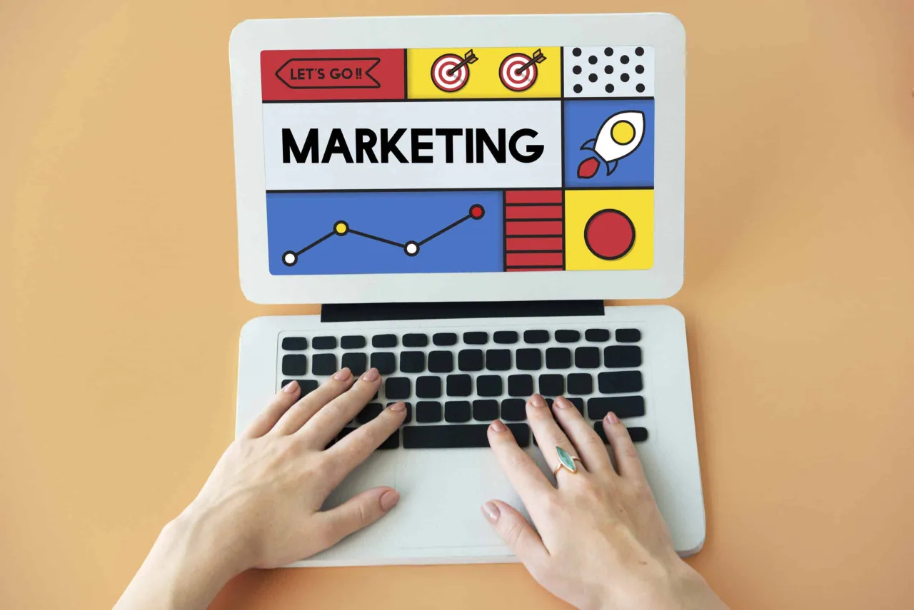 Ręce na klawiaturze laptopa, na ekranie napis MARKETING i grafiki symbolizujące sukces. Pamiętaj, że content is the king!