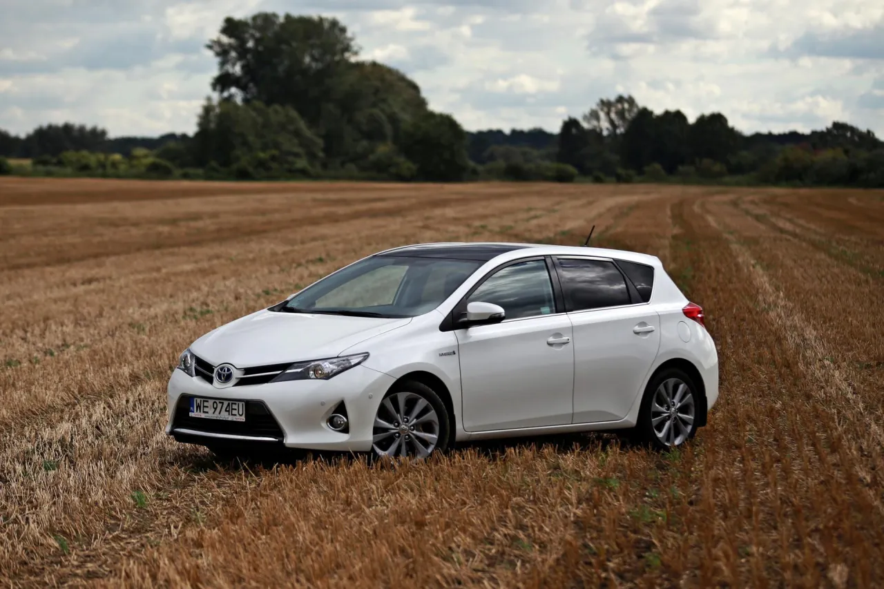 Biała Toyota Auris Hybrid na tle jesiennego pola. Zastanawiasz się, ile pali Toyota Auris Hybrid? Ten model zachwyca niskim spalaniem.