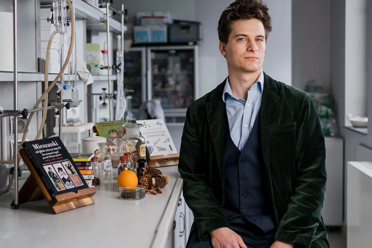 Młody mężczyzna w laboratorium, obok niego książka 