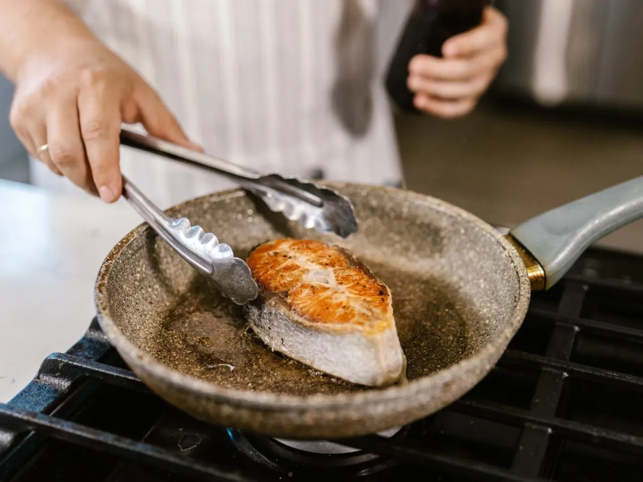 Kucharz sprawdzający widelcem usmażoną rybę