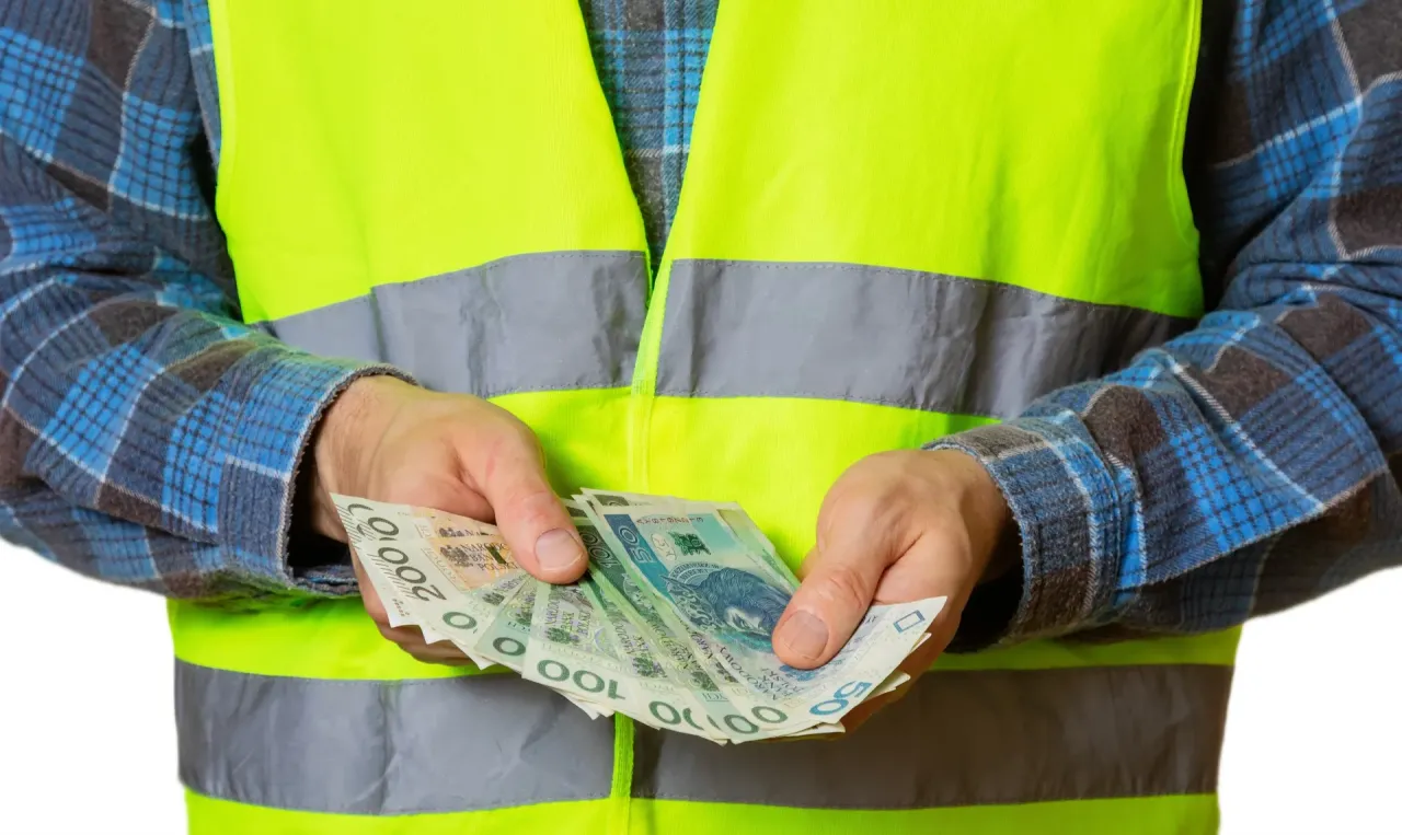 Pracownik w kamizelce odblaskowej trzyma w rękach polskie banknoty. Czy to odpowiedź na pytanie, ile wynosi fundusz socjalny na jednego pracownika?