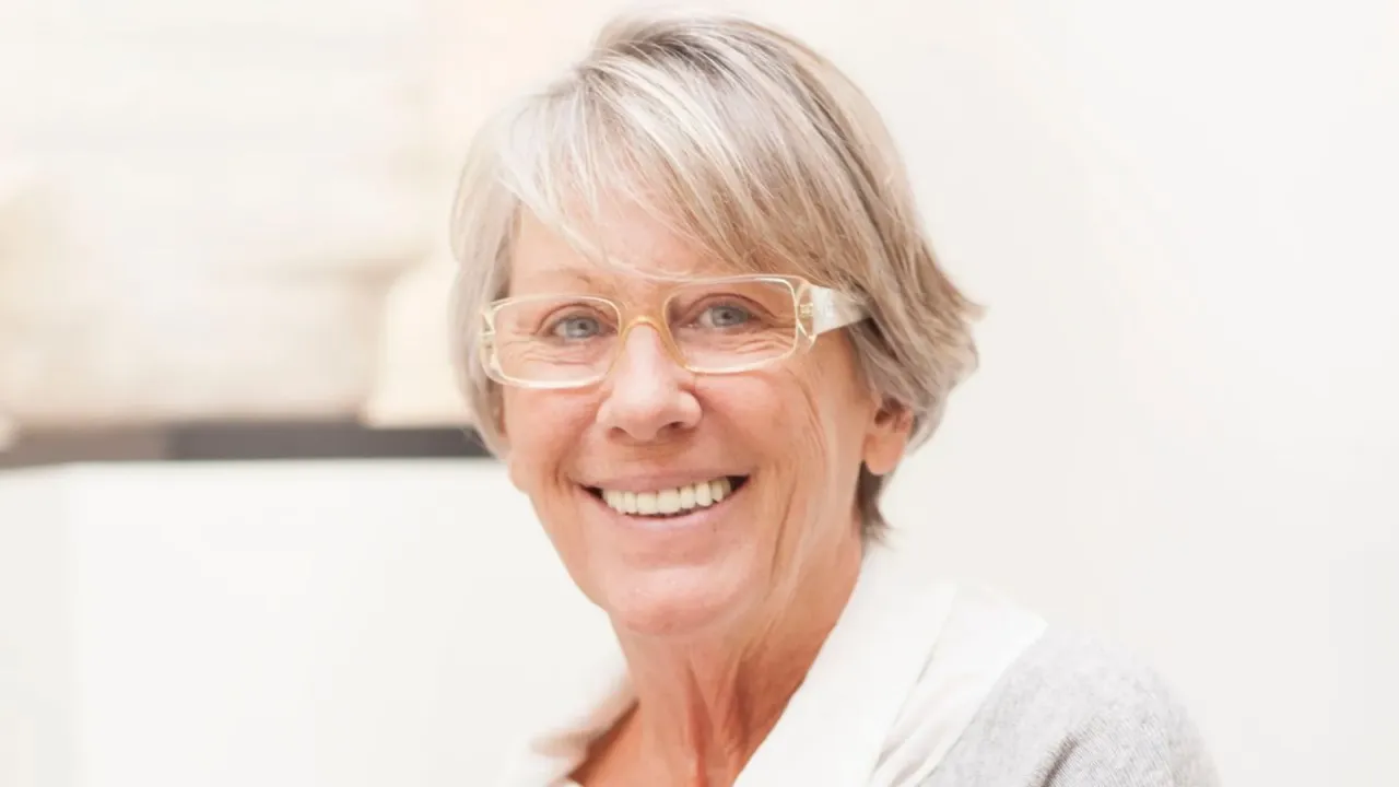 Uśmiechnięta starsza pani w okularach, zastanawiająca się, czy technikum wlicza się do stażu pracy do emerytury.