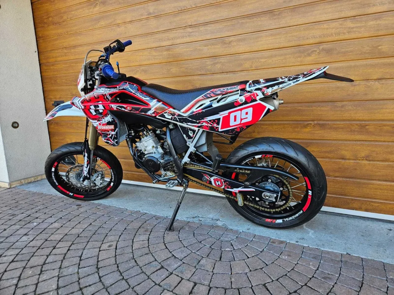 Agresywny Husqvarna 125 supermoto w czerwono-czarnej grafice, gotowy do akcji na ulicy.