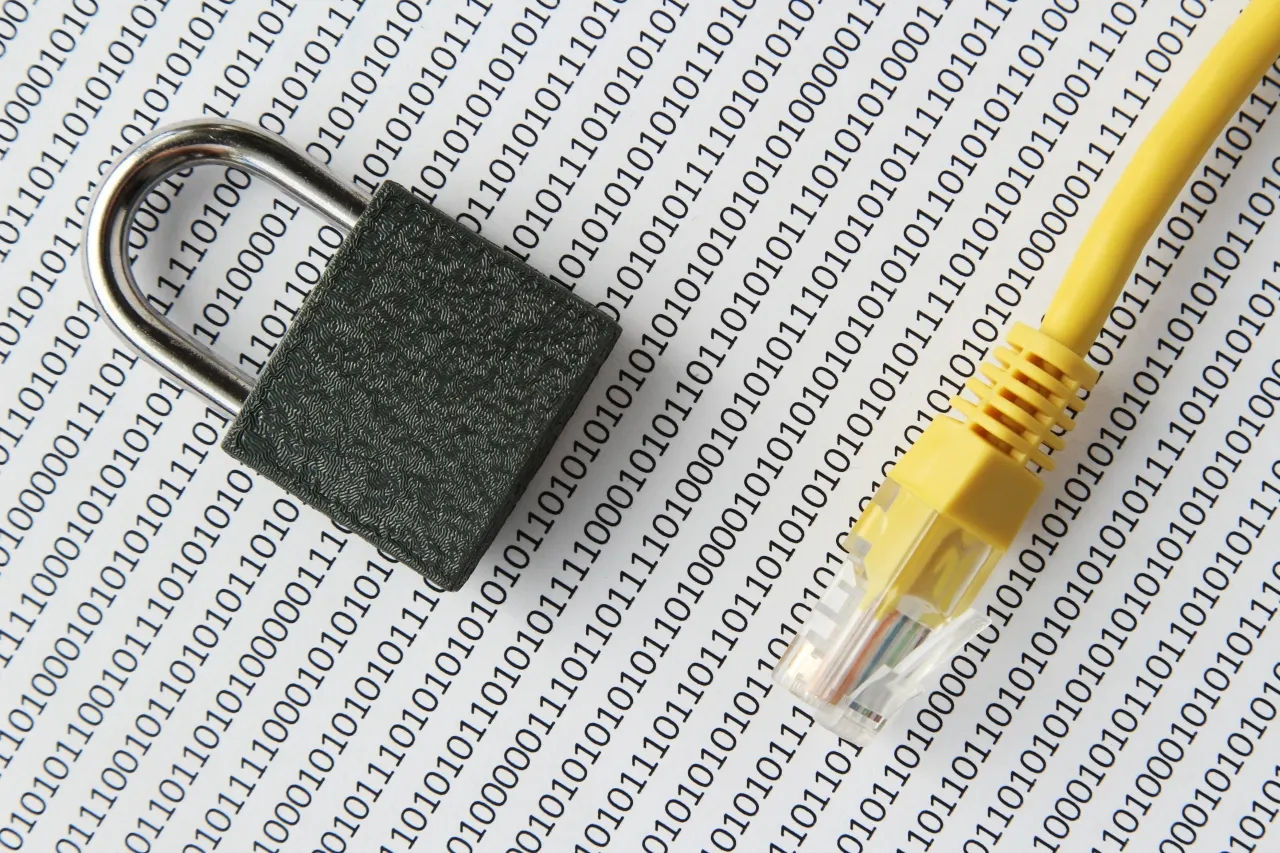 Kł&oacute;dka i kabel sieciowy na tle kodu binarnego symbolizują szyfrowanie pendrive i bezpieczeństwo danych.