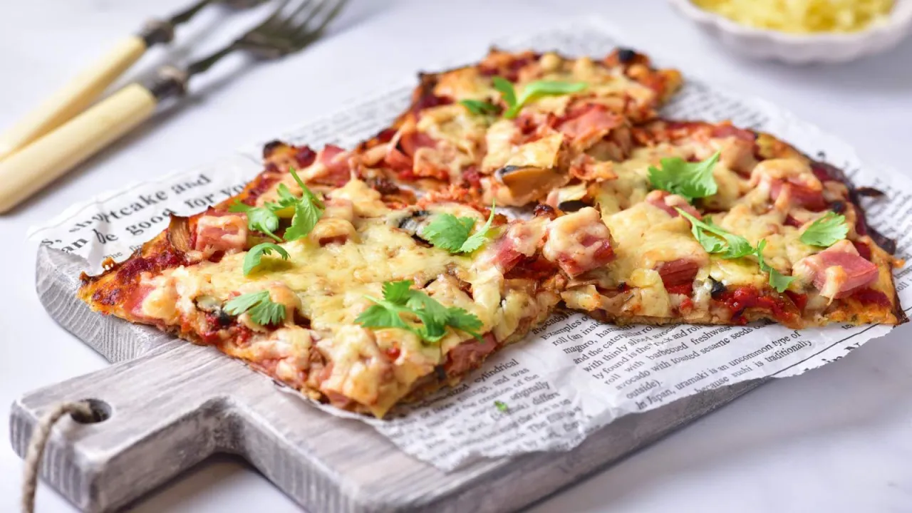 Pyszna pizza z szynką i serem, ozdobiona świeżymi ziołami. Idealna do podania, gdy zastanawiasz się, co zrobić z oregano.