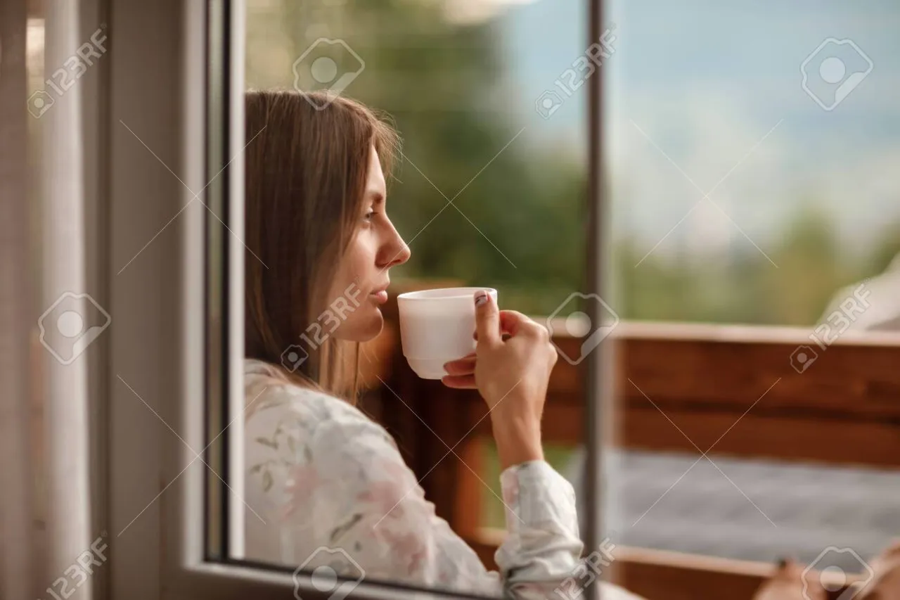 Osoba pijąca szklankę wody i patrząca przez okno rano