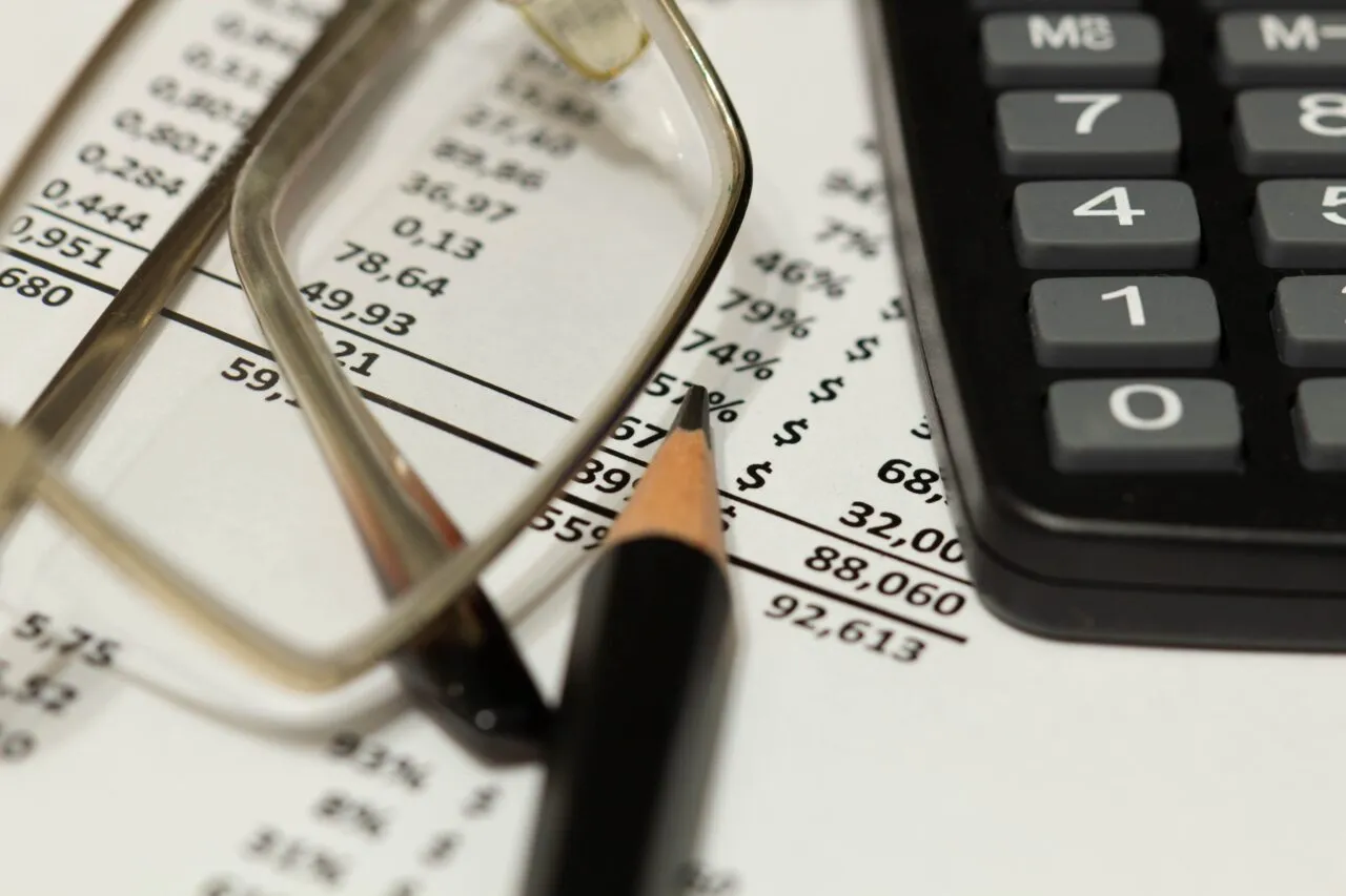 Okulary, oł&oacute;wek i kalkulator na arkuszu z danymi liczbowymi. Jak sprawdzić czy firma ogłosiła upadłość?