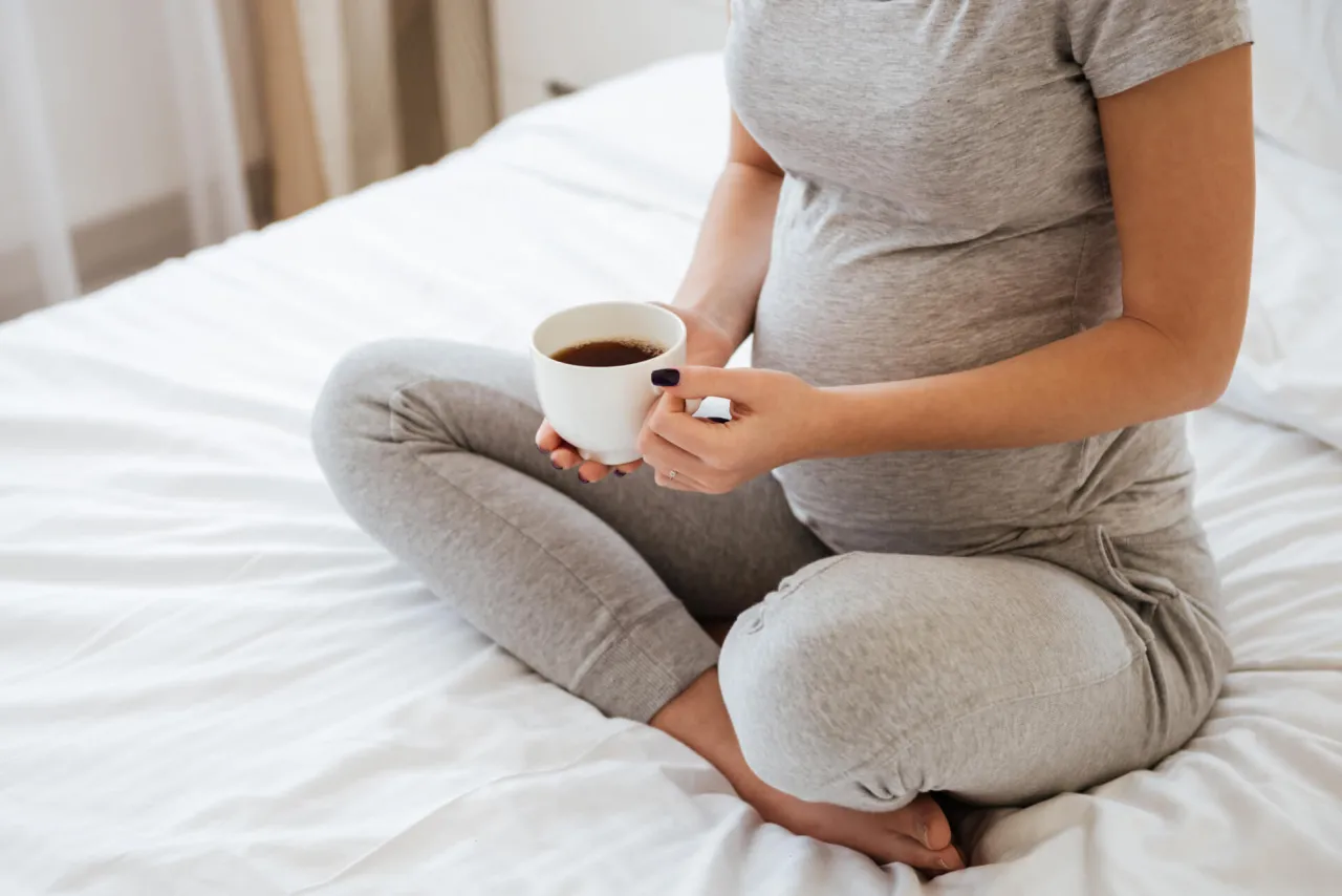 Ciężarna kobieta pijąca kawę, bezpieczna ilość kofeiny w ciąży infografika
