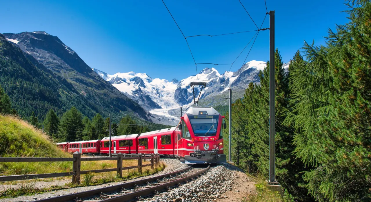 Czerwony pociąg mknie przez alpejski krajobraz. Marzysz o podróży, gdzie pociągiem z Warszawy dotrzesz do takich widoków?