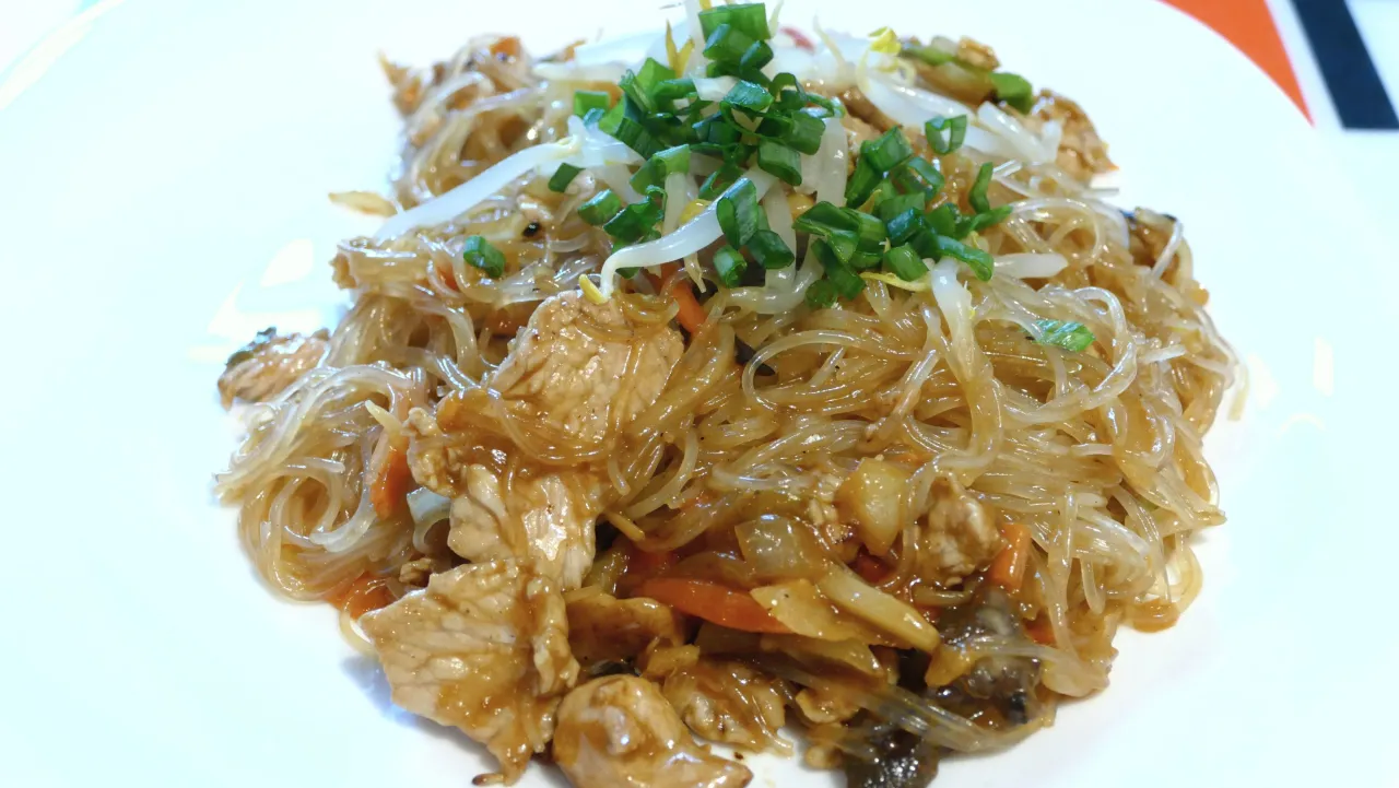 Pyszny makaron sojowy jak gotować: danie z kurczakiem, warzywami i kiełkami fasoli mung, posypane szczypiorkiem.