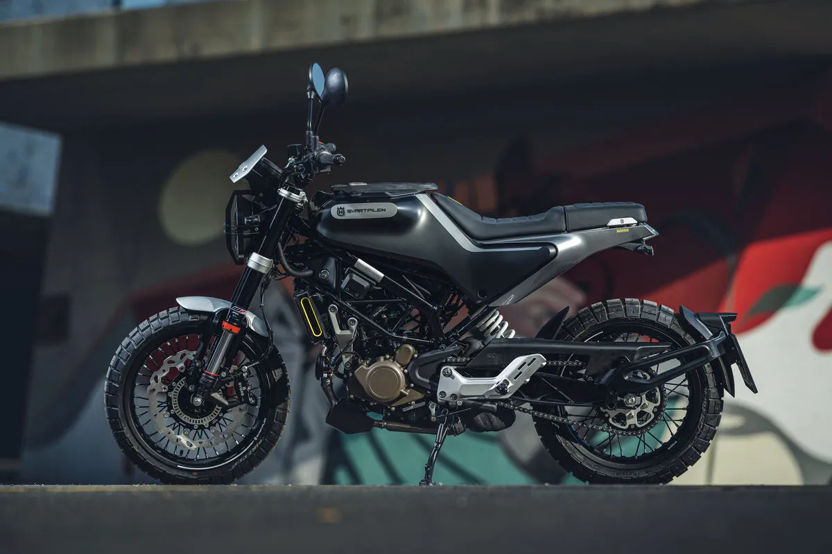 Stylowy motocykl Husqvarna 125 4t w ciemnej kolorystyce, zaparkowany na tle graffiti.