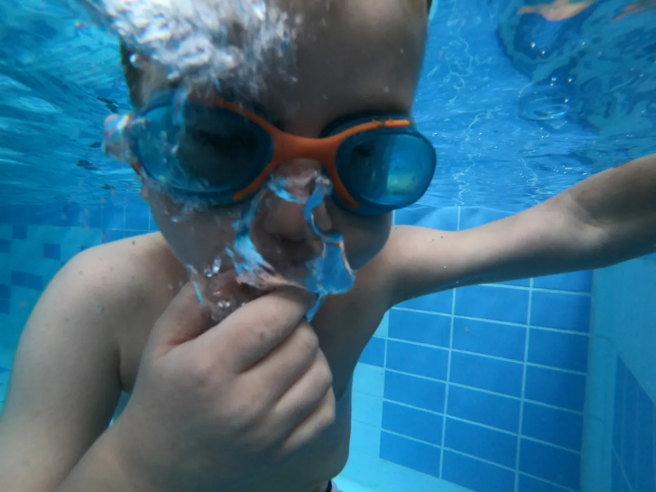 Chłopiec w goglach pod wodą, uczący się pływać. Czas nauki pływania zależy od dziecka.