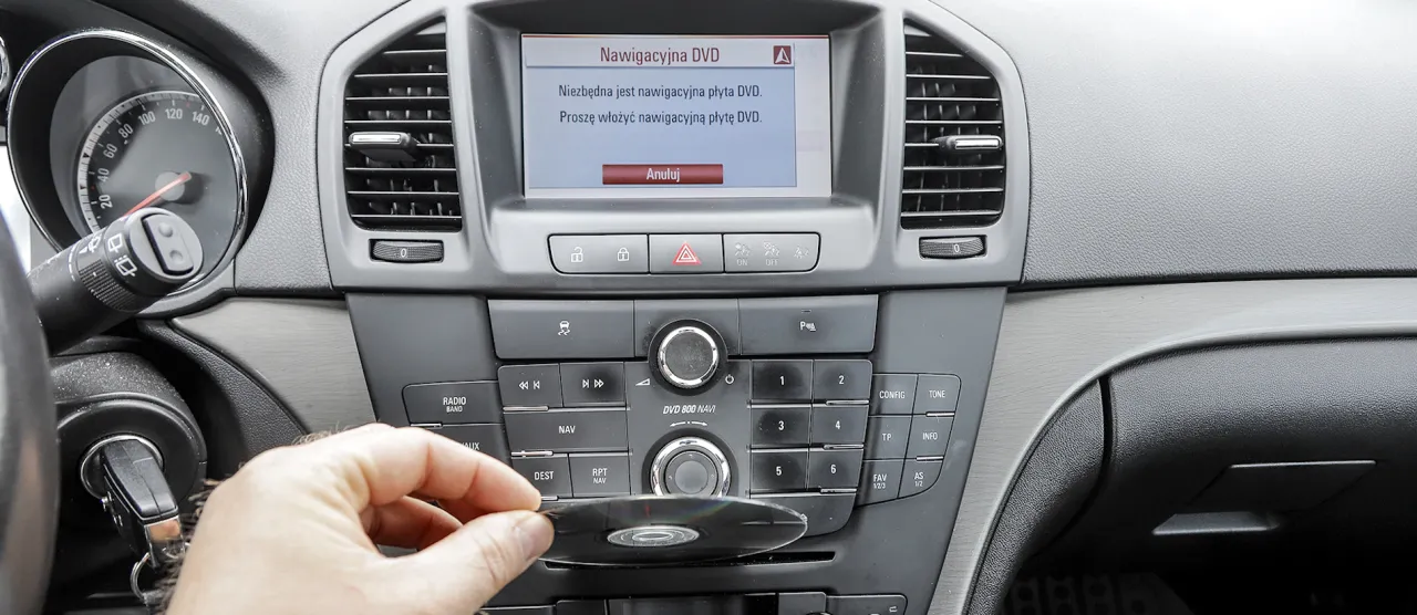 Ręka wkłada płytę DVD do nawigacji, by zaktualizować mapę. Na ekranie komunikat: 