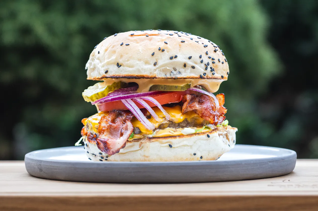 Soczysty burger z bekonem, serem i warzywami. Idealny przykład, jak jeść burgera, by poczuć pełnię smaku.