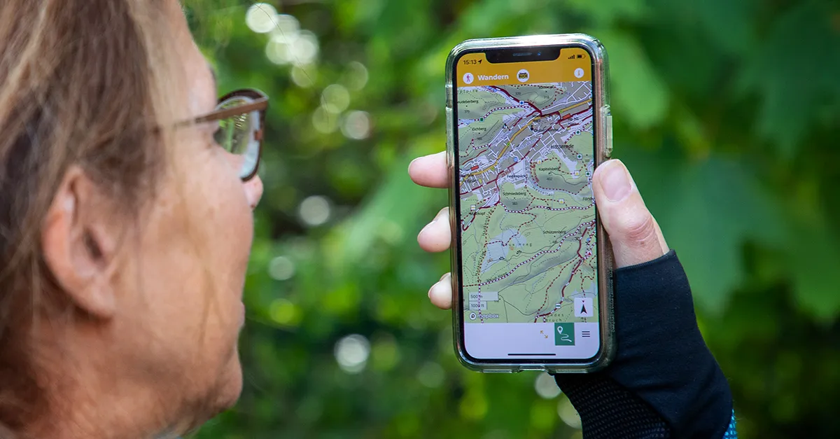 Wanderer schaut auf eine digitale Wanderkarte auf dem Smartphone in den Bergen
