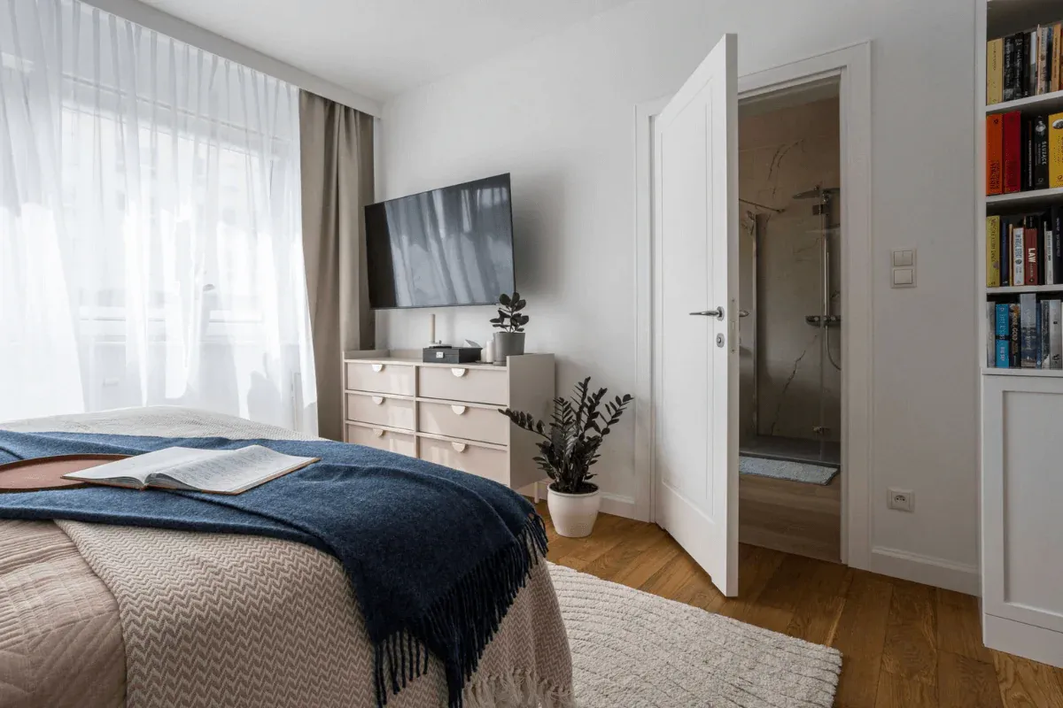 Przytulna sypialnia z wygodnym ł&oacute;żkiem, telewizorem i książkami. Idealne miejsce, by dowiedzieć się, jak urządzić pok&oacute;j dla seniora.