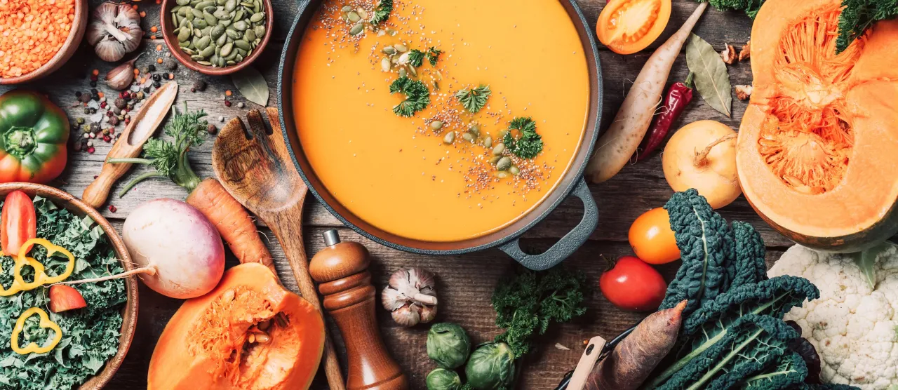 Zupa dyniowa i świeże warzywa na drewnianym stole. Zdrowe jedzenie to spos&oacute;b, jak zmniejszyć zanieczyszczenie środowiska.