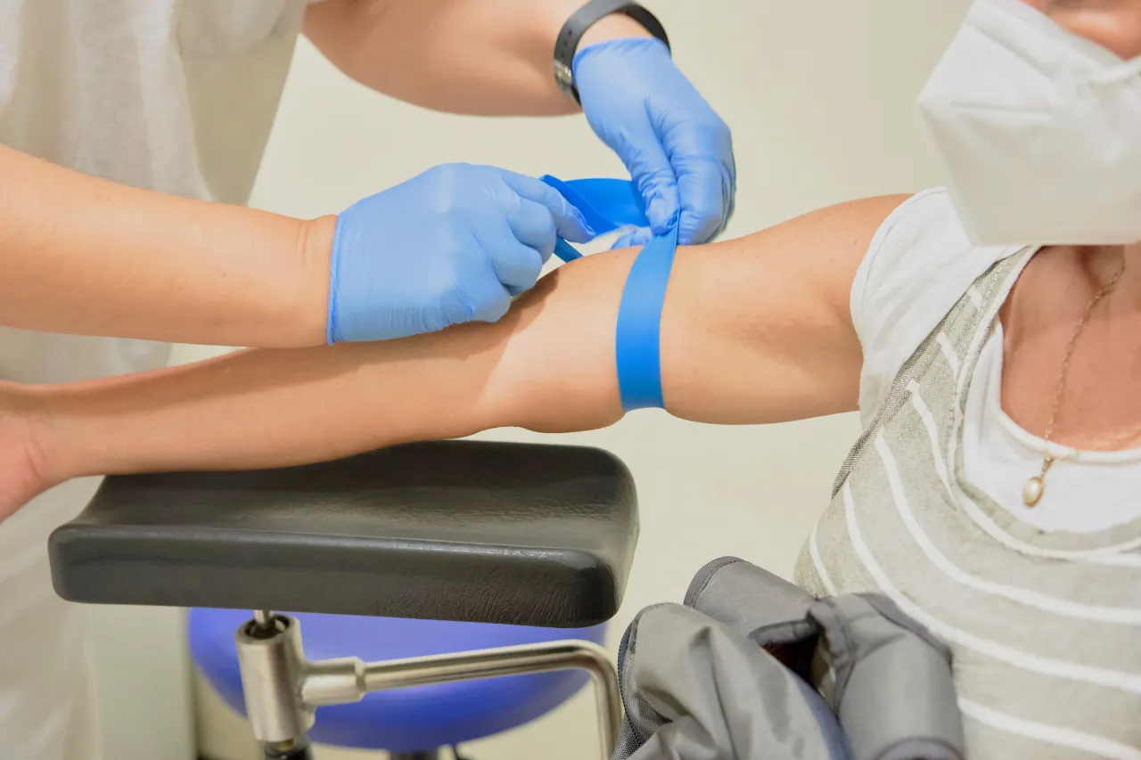 Pobieranie krwi do badań immunologicznych. Ręka pacjenta z założonym stazą, pielęgniarka w rękawiczkach przygotowuje się do wkłucia.